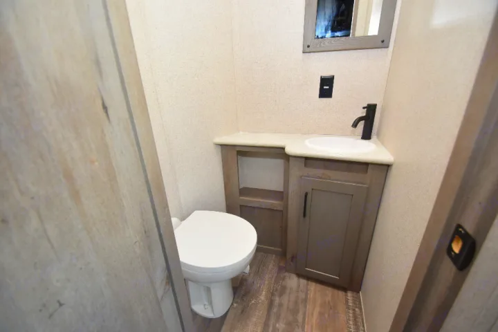 Clean RV rental bathroom with compact toilet, sink vanity, mirror, and modern wood-look flooring.. Keystone Raptor 2025
