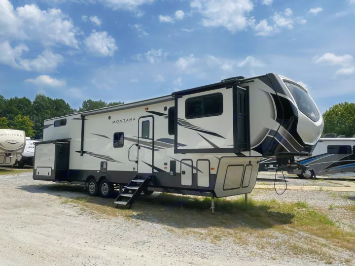 A large white and black Montana fifth-wheel RV with extended slide-outs, parked on a gravel lot, ready for RV rental.. Keystone RV Montana High Country 2024
