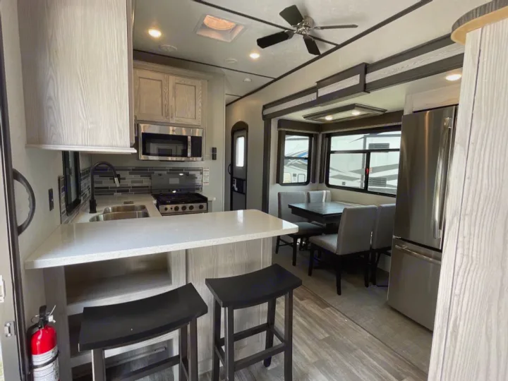 An RV rental's modern interior with a well-equipped kitchen, stainless steel fridge, bar seating, and a dining booth.. Keystone RV Montana High Country 2024