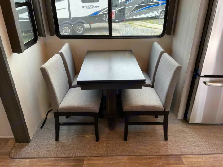 Enjoy meals in this RV rental's dinette: a dark table and four comfy, light-grey chairs. Windows offer outdoor views.. Keystone RV Montana High Country 2024