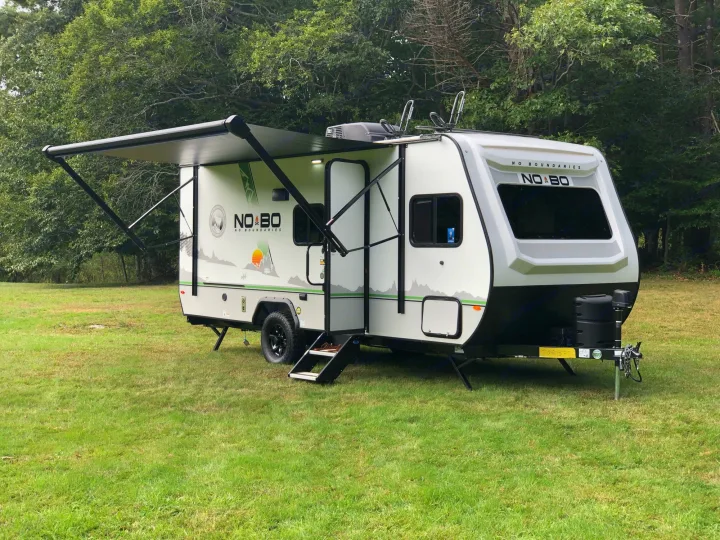 This light grey NO BO RV rental is set up in a green field, ready for outdoor adventures and camping.. No Boundaries 19 2021