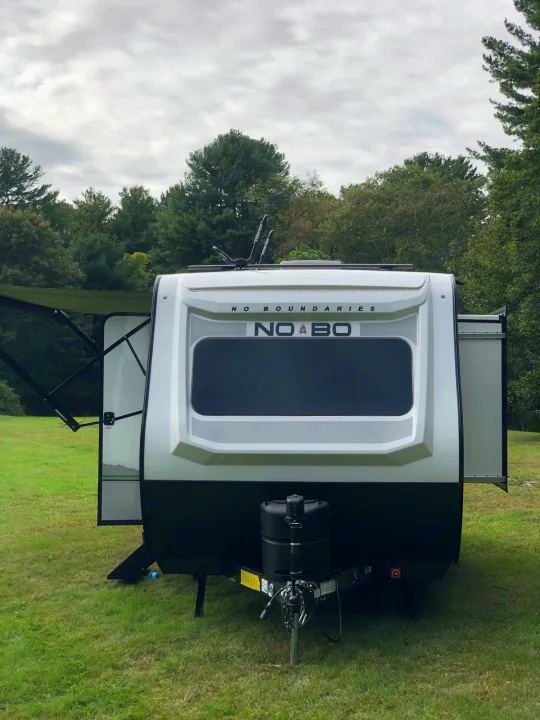 Modern white and black travel trailer RV, ideal for an rv rental getaway. Set on lush grass with a wooded backdrop.. No Boundaries 19 2021