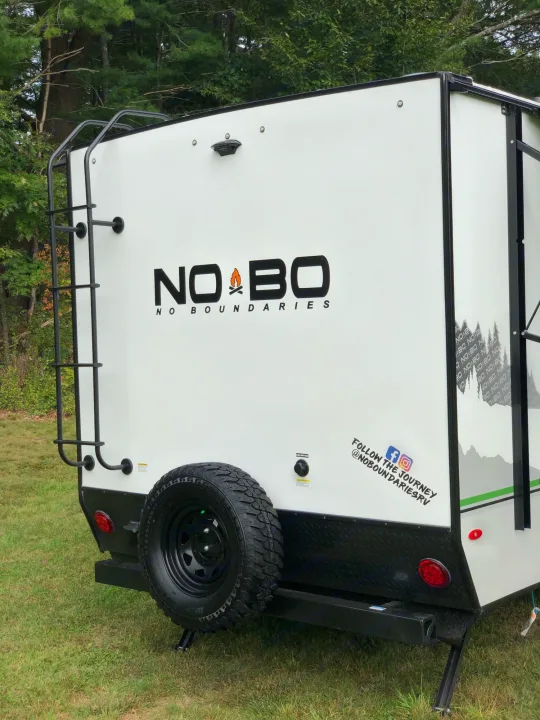 Rear view of a white No Boundaries RV rental camper with a ladder and spare tire, ready for outdoor adventure.. No Boundaries 19 2021