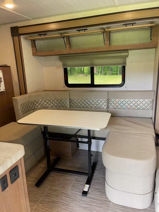 Cozy RV rental dinette features U-shaped quilted seating, adjustable table, overhead storage, and scenic window views.. No Boundaries 19 2021