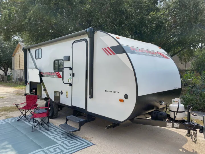 A white Platinum Wildwood FSX travel trailer, perfect for your next RV rental adventure, with outdoor mat and chairs.. Forest River Wildwood 2021