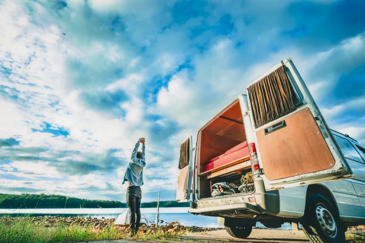 A person stretches beside their **rv rental** with open rear doors, by a tranquil lake.. Mercedes-Benz Sprinter 2005