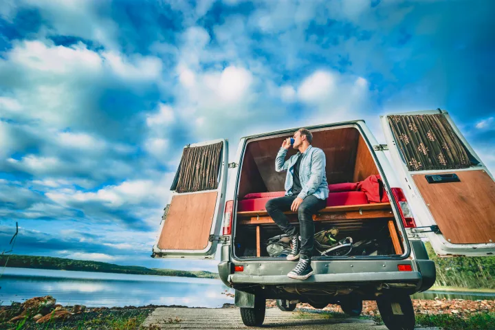Enjoy nature with an **RV rental**! A man sips coffee from his camper van, parked by a tranquil lake under a blue sky.. Mercedes-Benz Sprinter 2005