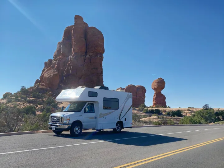 White RV rental parked on a scenic desert road, framed by towering red rock formations under a clear blue sky.. Thor Motor Coach Four Winds Majestic 2017