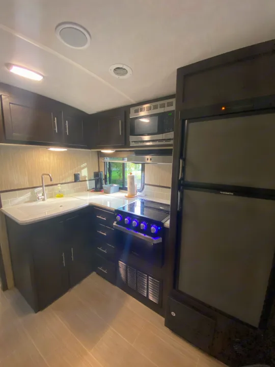 A bright, organized RV rental kitchen showcasing dark cabinetry, modern appliances like a Dometic fridge, stove, microwave, and sink.. Cruiser Rv Corp Fun Finder 2018