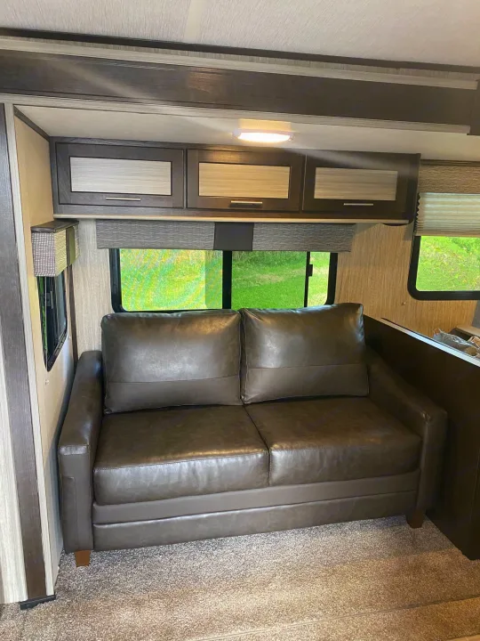 A comfortable dark brown leather couch inside an RV rental, with modern cabinetry and large windows showing lush greenery.. Cruiser Rv Corp Fun Finder 2018