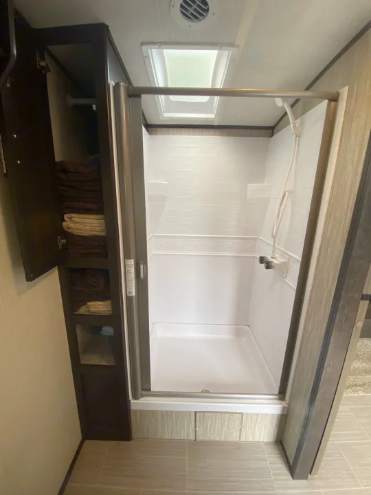 Interior of an RV rental showing a white shower stall with skylight and a tall, dark wood linen cabinet.. Cruiser Rv Corp Fun Finder 2018