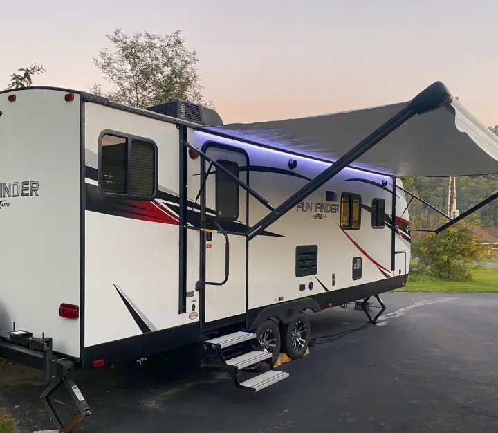 Modern white rv rental with blue LED awning lights extended, parked on an asphalt surface.. Cruiser Rv Corp Fun Finder 2018