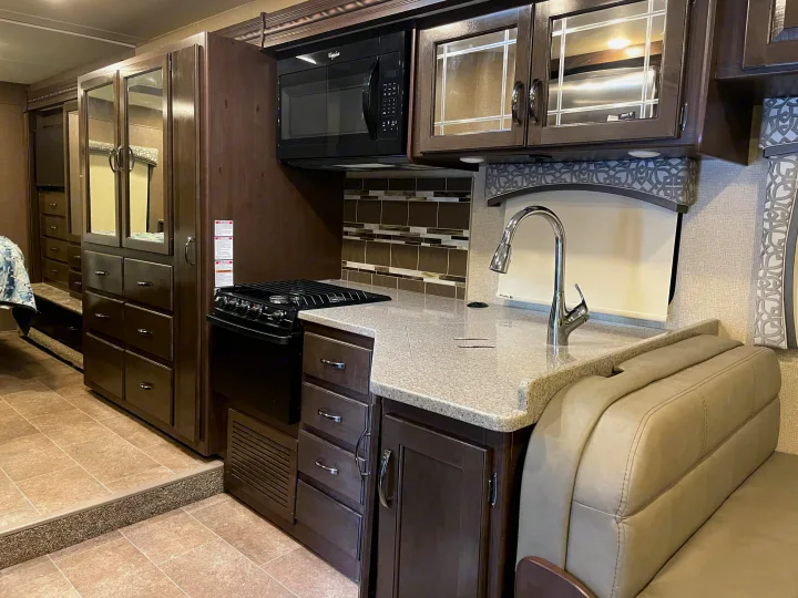 An RV rental kitchen featuring light counters, a sink, microwave, stove, and ample dark wood cabinetry.. Thor Motor Coach Chateau 2017