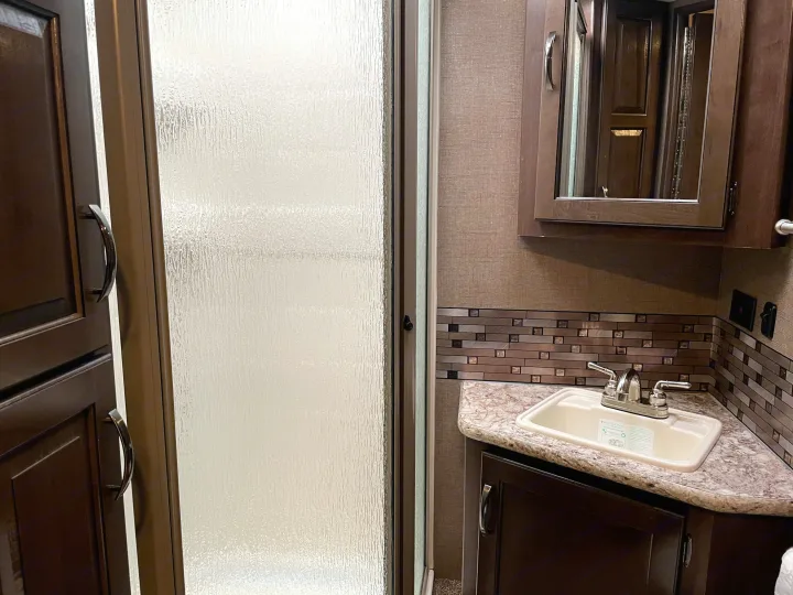 This RV rental bathroom features a compact shower with frosted glass, a sink vanity, and a mirrored cabinet.. Thor Motor Coach Chateau 2017