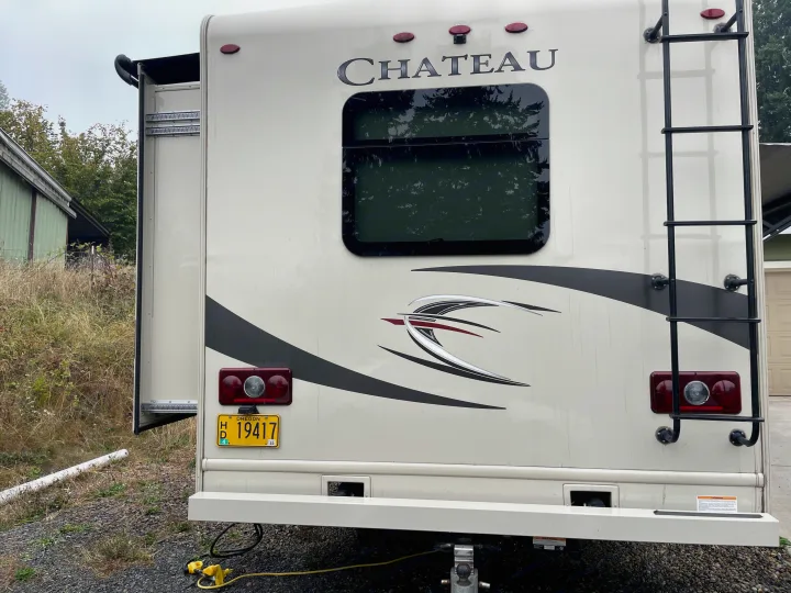 Rear view of a cream Chateau motorhome, with its slide-out extended, ladder, and Oregon license plate, ready for RV rental.. Thor Motor Coach Chateau 2017