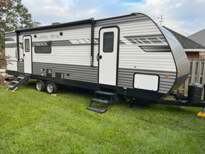 This grey and white Aspen Trail travel trailer RV rental is parked on grass, featuring two entry doors with steps.. Dutchmen Aspen Trail 2021