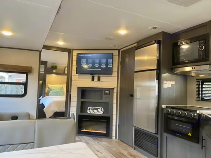 Bright RV rental interior features a cozy living area with TV/fireplace, full kitchen, and glimpse of a bedroom.. Dutchmen Aspen Trail 2021