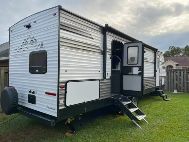 Aspen Trail RV rental, a travel trailer with open door and steps, parked on grass with a rear spare tire.. Dutchmen Aspen Trail 2021