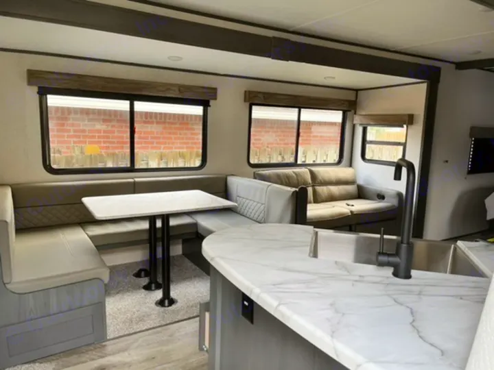 Inside a modern RV rental: a bright living space with a U-shaped dinette, sofa, and a kitchen featuring a white marble counter.. Dutchmen Aspen Trail 2021