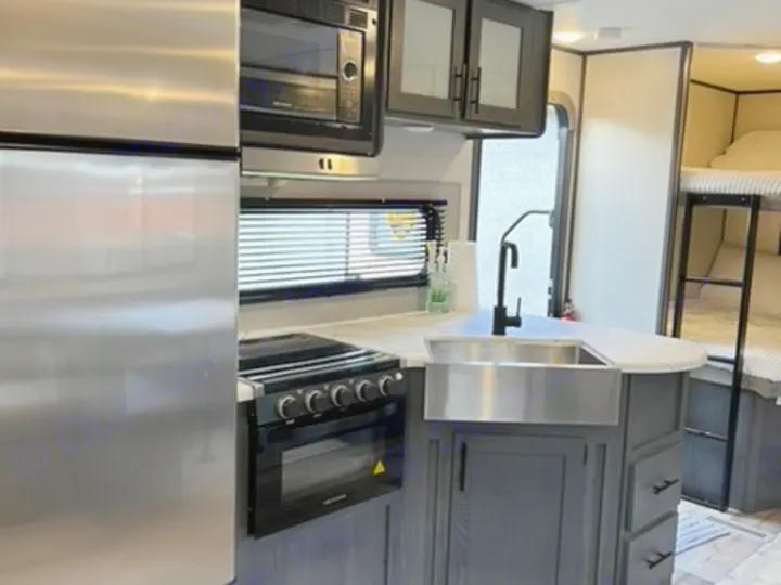 Modern rv rental kitchen with stainless appliances, sink, oven, and bunk beds visible for comfortable family travel.. Dutchmen Aspen Trail 2021