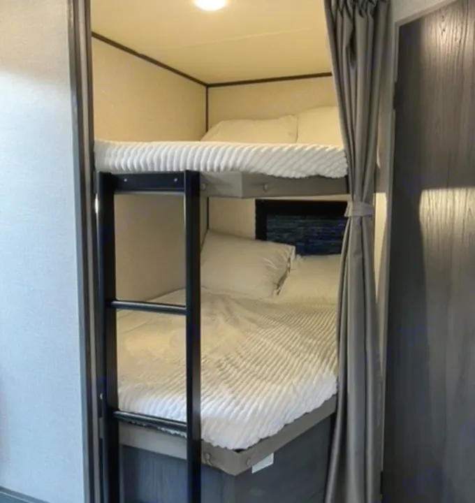 Discover comfortable sleeping in this RV rental's bunk beds. Features include a ladder, soft white bedding, and compact design.. Dutchmen Aspen Trail 2021