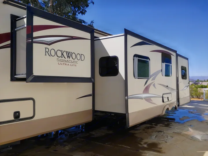 A large beige Rockwood Signature RV with extended slide-outs, ready for an RV rental adventure. Parked on wet concrete.. Forest River Rockwood Signature Ultra Lite 2017