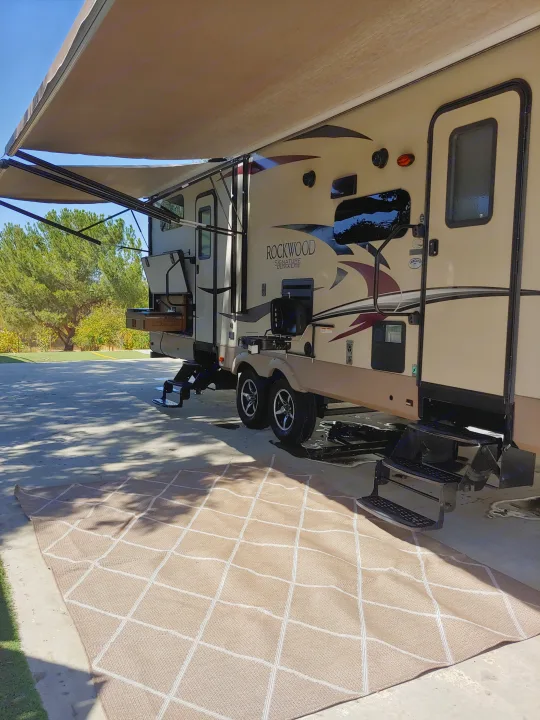 Tan Rockwood RV rental with awning, outdoor kitchen, steps, and patterned rug at a sunny campsite.. Forest River Rockwood Signature Ultra Lite 2017