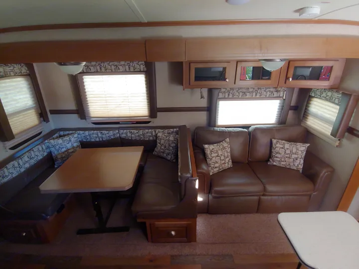 Spacious RV rental interior featuring a brown dinette, matching sofa, overhead cabinets, and large windows with blinds.. Forest River Rockwood Signature Ultra Lite 2017