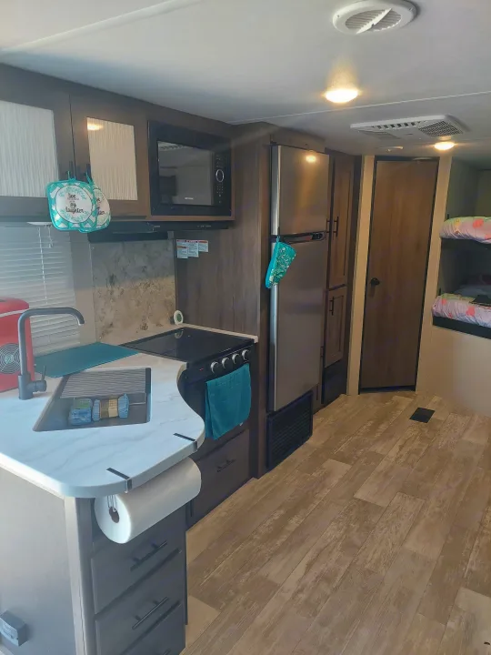 RV rental: A compact, modern interior showcasing a kitchen with microwave, fridge, stove, sink, and comfortable bunk beds.. Prime Time Avenger 2021