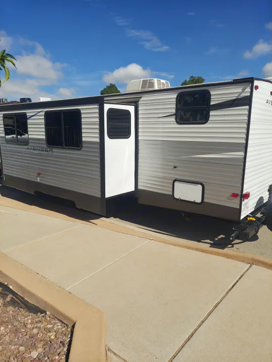 A travel trailer (rv rental) with its door open, parked under a bright blue sky on a sunny day.. Prime Time Avenger 2021