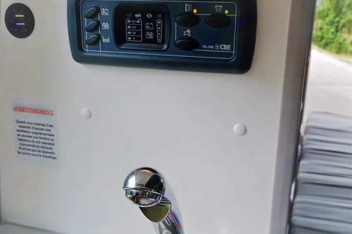 An rv rental's interior setup: a CBE PC-100 control panel displaying levels, USB ports, a kitchen faucet, and a safety warning.. Volkswagen Transporter T6.1 2022