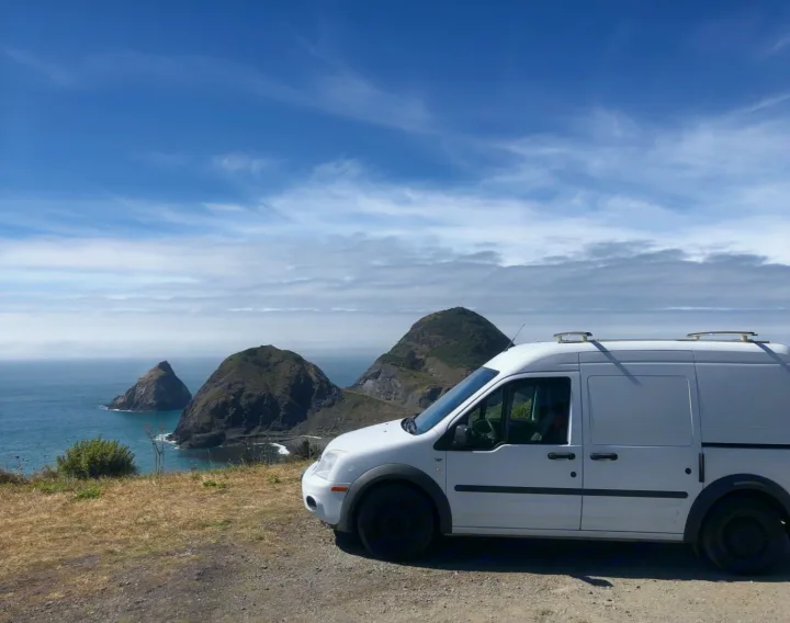 Scenic **RV rental** adventure: A white camper van parked at a stunning coastal overlook with majestic sea stacks and blue ocean.. Ford Connect 2012