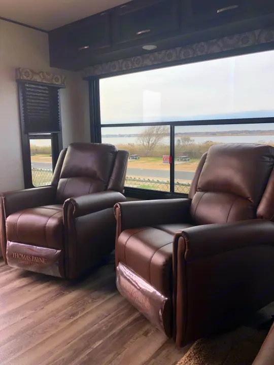 Inside an RV rental, two brown recliners offer comfort with a scenic window view of a bay. Thomas Payne Collection chairs.. Jayco Jay Flight 2020