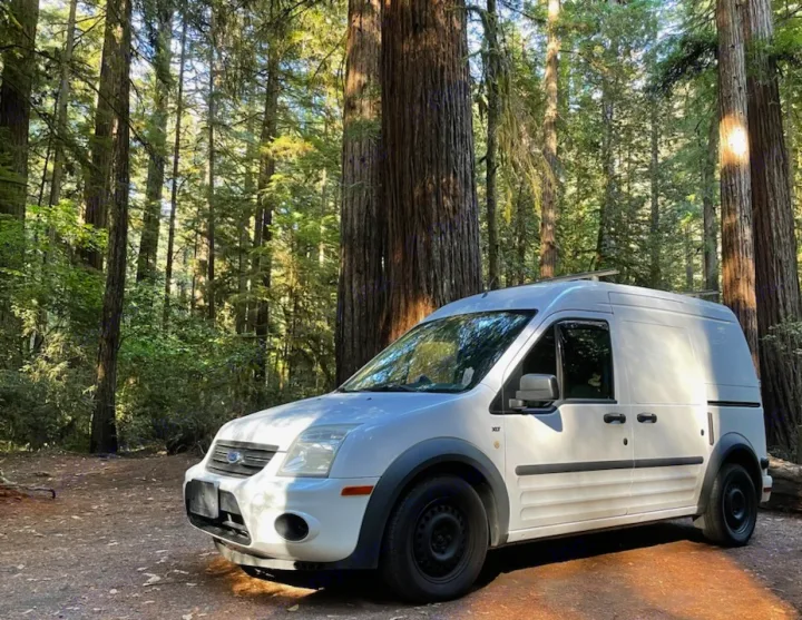 White Ford Transit Connect van, ready for RV rental, parked in a towering redwood forest.. Ford Connect 2012