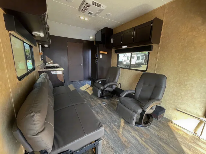 Spacious RV rental interior features recliners, a couch, kitchenette, and overhead cabinets for comfortable travel.. Dune Sport Toy Hauler 2017