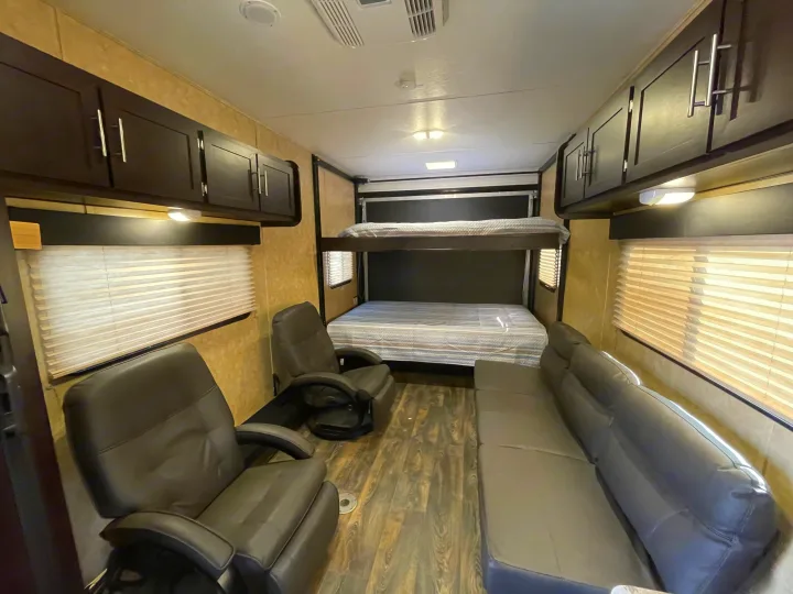 Spacious rv rental interior with a bunk bed, two recliners, and a sofa, featuring overhead cabinets and wood-look flooring.. Dune Sport Toy Hauler 2017