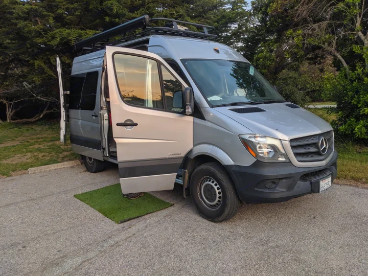 Silver Mercedes Sprinter RV rental van parked. Its side door is open with a green mat, ready for adventure.. Mercedes-Benz Sprinter 2016