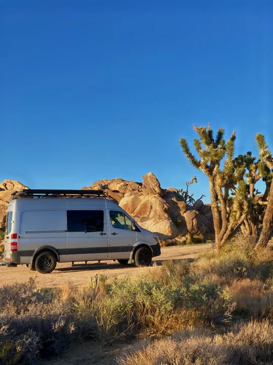 Silver Sprinter van (RV rental) parked among Joshua trees and rocks in a desert setting.. Mercedes-Benz Sprinter 2016