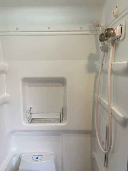 RV rental's compact bathroom with white shower stall, handheld shower, shelf, and Thetford toilet.. Winnebago Solis 2021