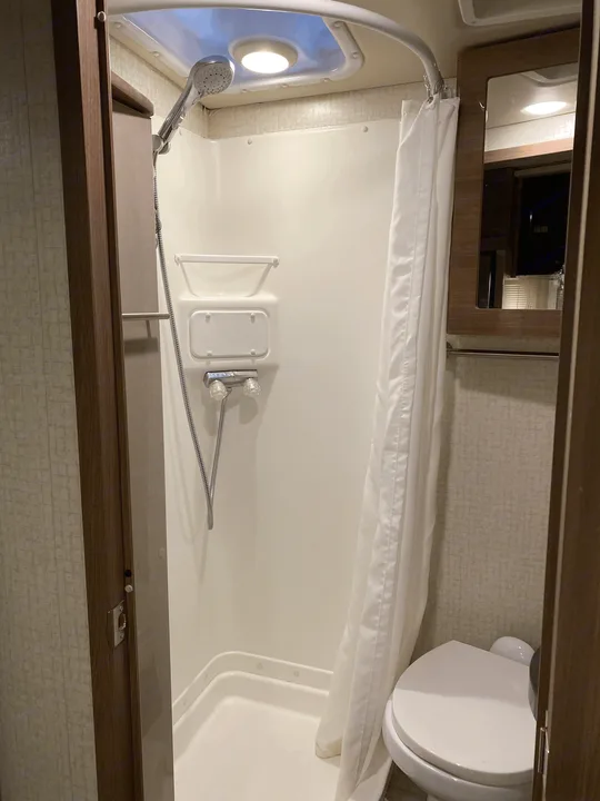 Compact RV rental bathroom features an enclosed shower, toilet, & overhead light.. Winnebago View 2016