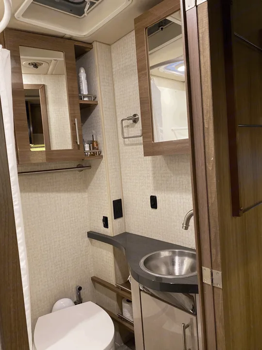 Compact RV rental bathroom with a stainless steel sink, mirror cabinet, toilet, and shower curtain.. Winnebago View 2016