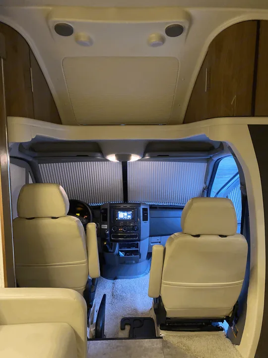 Inside an rv rental, showcasing the beige driver and passenger seats, dashboard console, and front window blinds.. Winnebago View 2016