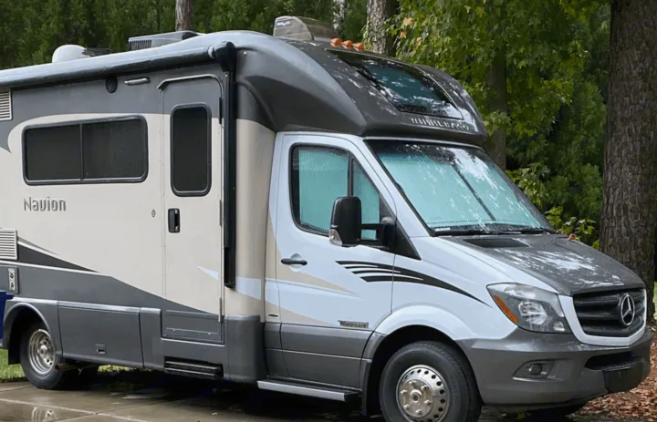 A white and grey Winnebago Navion RV, ideal for an rv rental adventure, parked outdoors on a paved surface.. Winnebago View 2016