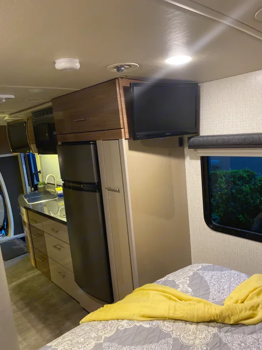 Inside a bright RV rental: kitchenette, refrigerator, microwave, wall-mounted TV, and cozy bed.. Winnebago View 2016