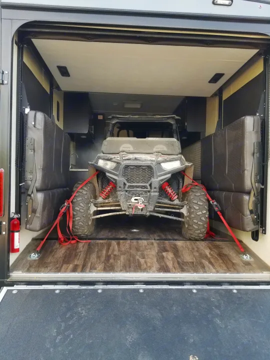 An RV rental toy hauler's interior shows a secured Polaris RZR UTV. The spacious cargo area features folded seats and a kitchen.. Jayco Octane 2017