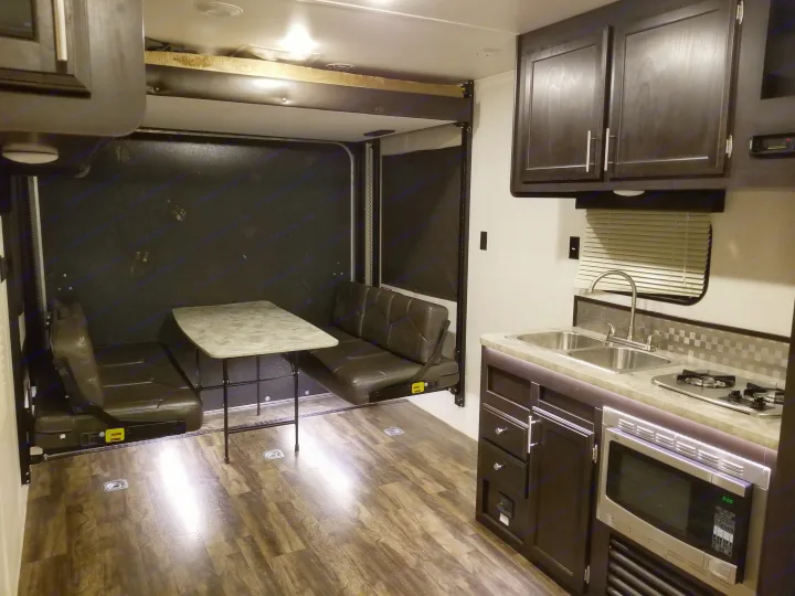 RV rental interior with kitchen, dual seating benches, portable table, and an elevated bunk bed.. Jayco Octane 2017