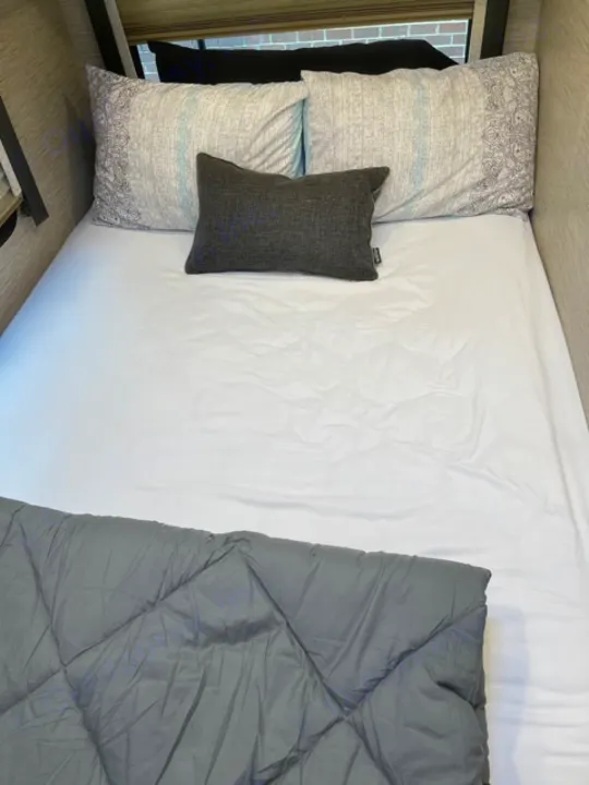 Relaxing RV rental bed: white sheets, patterned pillows, and a dark grey quilted comforter await.. Thor Motor Coach Four Winds 2022