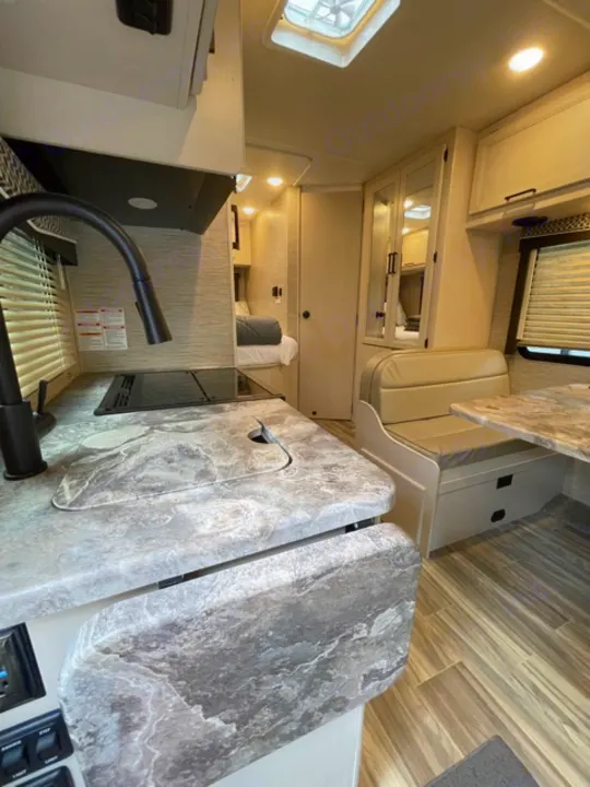 Inside a bright RV rental: modern kitchen with marbled counters, comfortable dinette, and wood-look flooring.. Thor Motor Coach Four Winds 2022