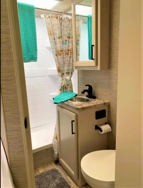 Step into this efficient RV rental bathroom, complete with a compact shower, vanity, toilet, and playful camper shower curtain.. Thor Motor Coach Four Winds 2022