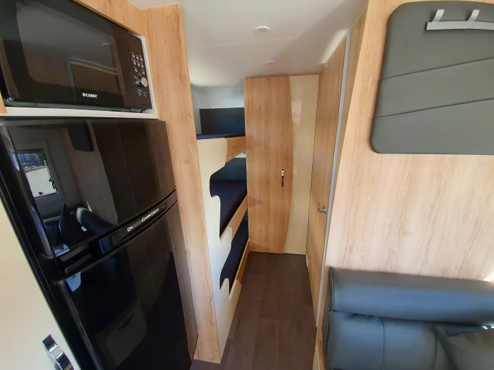 Compact RV rental interior featuring a microwave, fridge, bunk beds, and lounge seating, ideal for family travel.. Avan Aspire 617 Family 2021